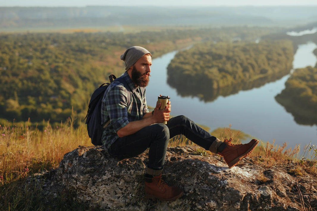 Image of person sitting on a rock, post hike, drinking a beverage through a flask